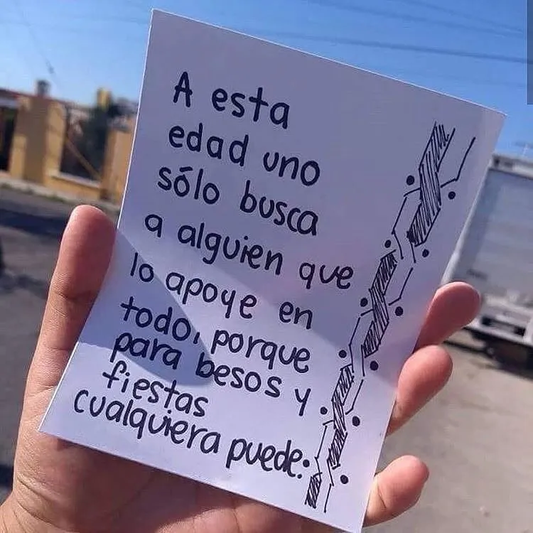 Una mano sostiene una hoja de papel blanco con un mensaje escrito a mano en español. El mensaje dice: "A esta edad uno solo busca a alguien que lo apoye en todo, porque para besos y fiestas cualquiera puede".